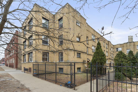 Front view of a multi-story brick apartment building with a gated entrance.
