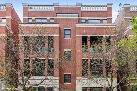 Front view of a multi-story brick building with balconies and decorative railing on the roof.