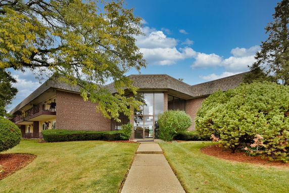 Front view of a two-story brick building with a sloped roof and large central glass entrance.