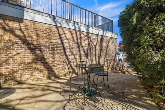 Outdoor patio area with a brick wall and metal railing, featuring a metal table and chairs.