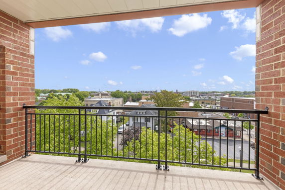 View from a building balcony overlooking a town with various buildings and green trees.
