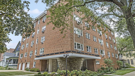 Front view of a multi-story brick building with multiple windows and ground level parking.
