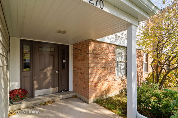 Front view of a brick house entrance with a covered porch and brown door.