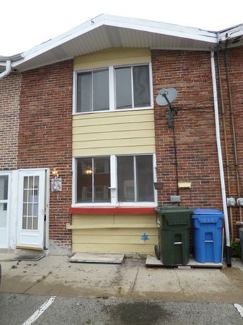 Front view of a two-story brick house with a satellite dish and garbage bins.