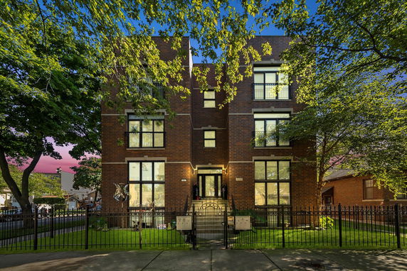 Front view of a three-story brick building with large windows and a gated front yard.