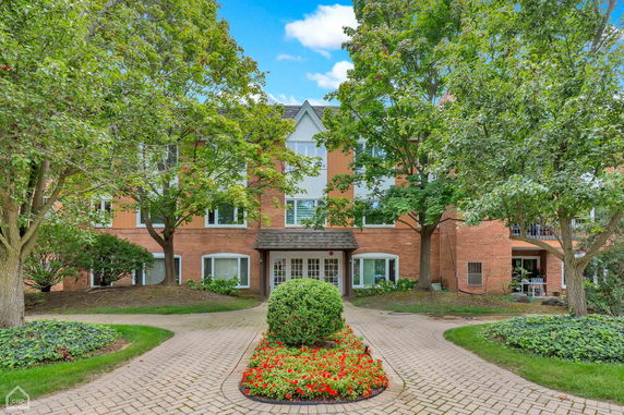 Front view of a multi-story brick building with large windows and a central entrance, surrounded by trees and landscaped gardens.