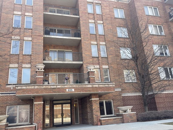 Front view of a multi-story brick apartment building with balconies and entrance.