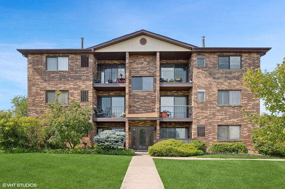 Front view of a three-story brick apartment building with balconies.