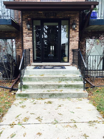 Front entrance of a brick building with metal railings and a glass door.