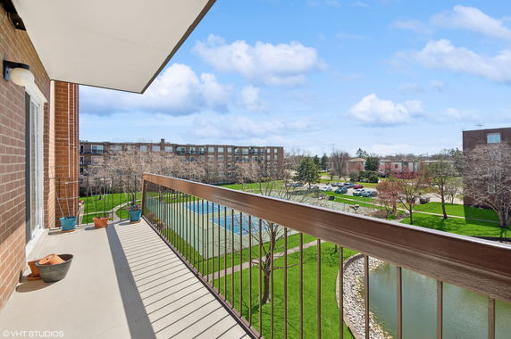 Balcony view from a building overlooking a tennis court and neighboring buildings.