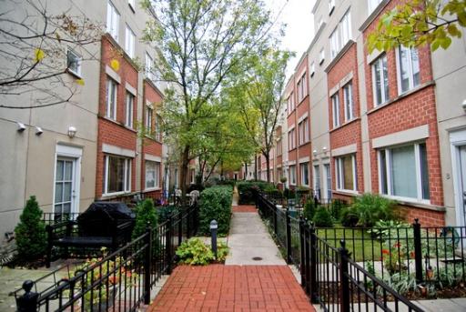 Exterior view of townhouse buildings with a central walkway lined with plants.