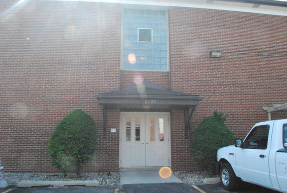 Front view of a brick building with a double door entrance and a large window above.