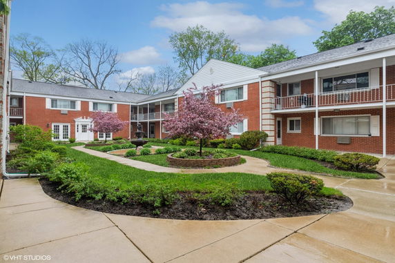View of an apartment complex with a landscaped courtyard featuring paths and blooming trees.