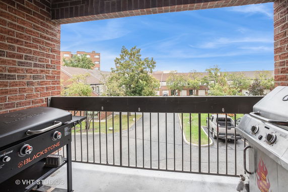View from a balcony with grills, overlooking a parking area and residential buildings.
