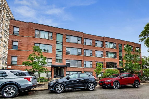 Front view of a multi-story brick building with several cars parked on the street.