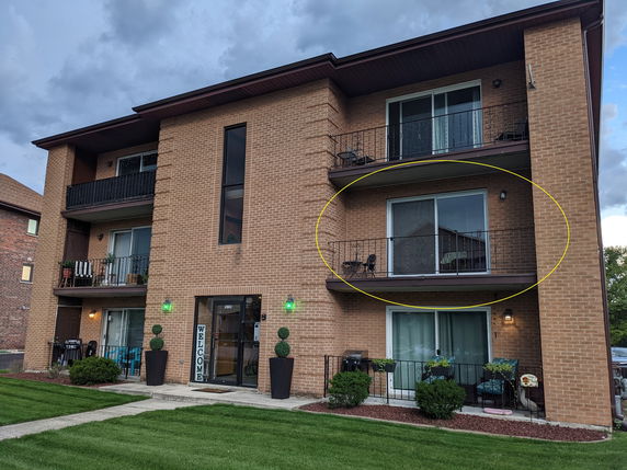 Front view of a three-story brick apartment building with balconies.