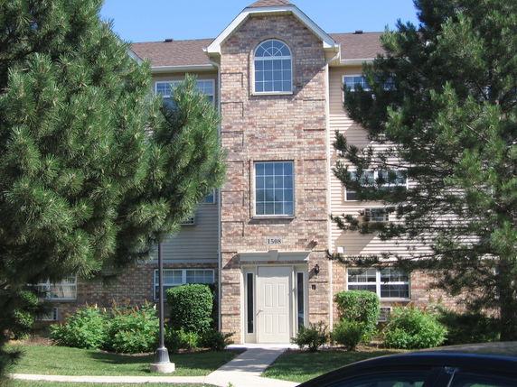Front view of a multi-story brick apartment building with trees on both sides.