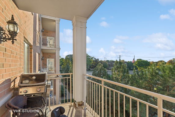 View from a balcony showing nearby trees and a building in the distance.