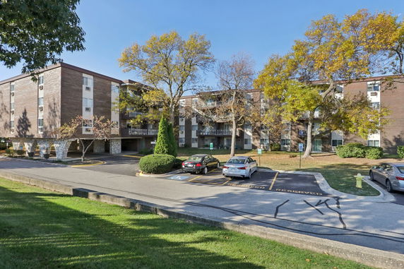 Front view of a multi-story apartment building with balconies and a parking area.