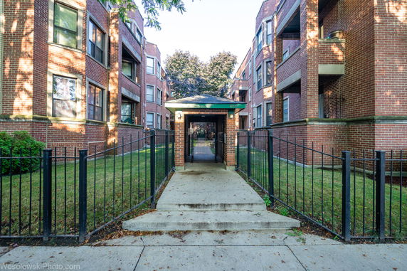 Front view of a multi-story apartment building with brick exterior and gated entrance.