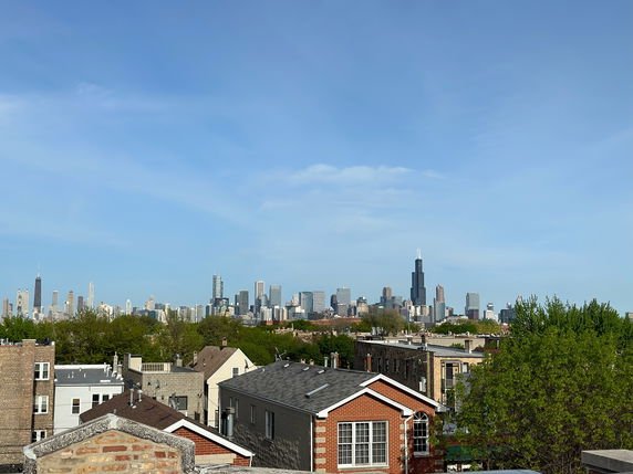 Panoramic view of a city skyline with skyscrapers and residential rooftops in the foreground.