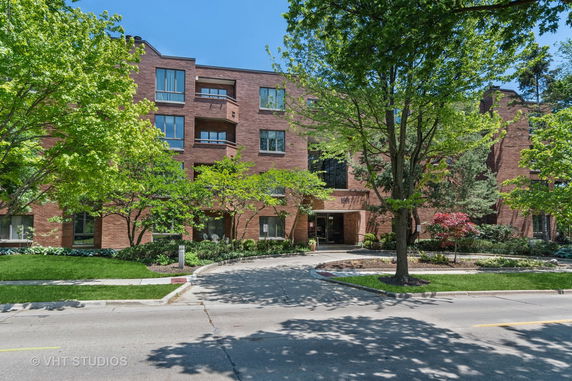 Front view of a multi-story brick building with large windows and a circular driveway.