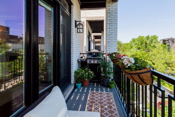 Balcony with plants and a grill, overlooking greenery and adjacent buildings.