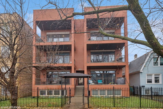 Front view of a multi-story brick building with balconies and a gated entrance.