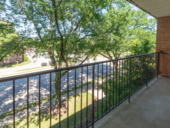 View of surrounding area from a balcony showing trees and a road.