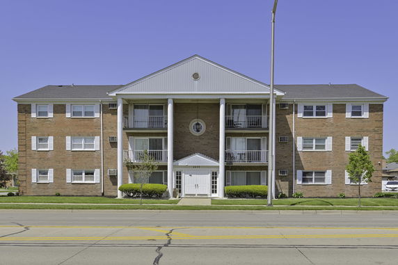 Front view of a three-story brick apartment building with white columns and a gable roof.