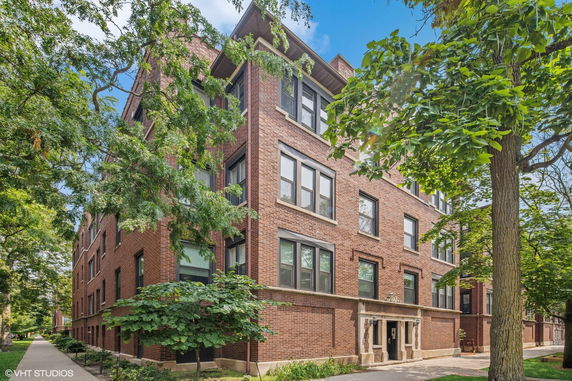 Front view of a three-story brick apartment building with several windows and trees nearby.