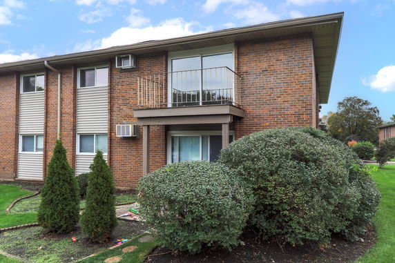 Front view of a two-story brick building with a balcony and air conditioning units.
