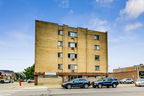 Front view of a multi-story brick building with multiple windows and parked cars in front.