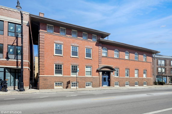 Front view of a multi-story brick building with a blue door and multiple windows.