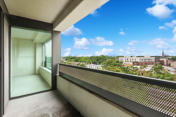 View of surrounding area from a balcony with buildings and trees in the distance.