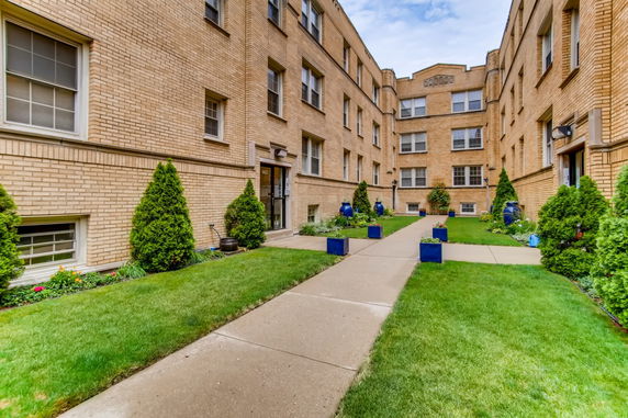 Front view of a brick apartment building with multiple stories and small landscaped courtyard.