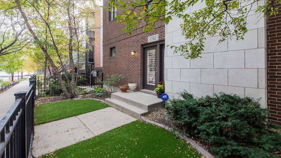 Front view of a brick house entrance with steps leading up to a door, surrounded by a small landscaped area.