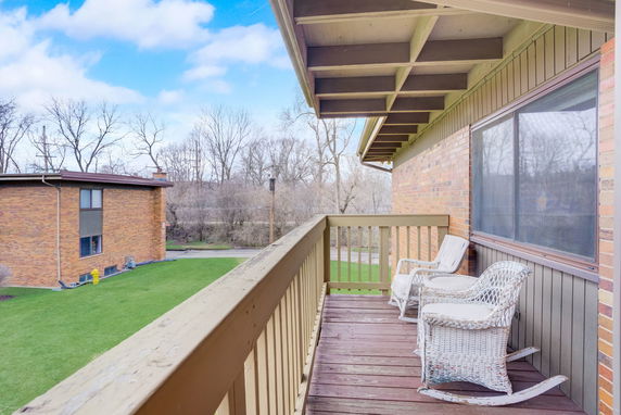 Wooden balcony with wicker chairs overlooking a lawn and trees.