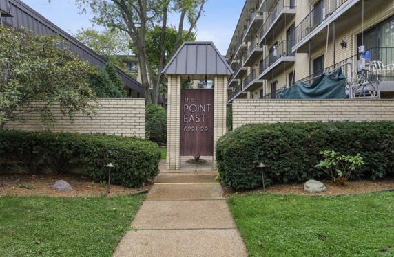 Front view of a multi-story residential building with balconies and a landscaped entrance.