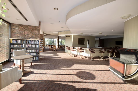 Interior of a clubhouse with a reading area, bar seating, and dining tables.