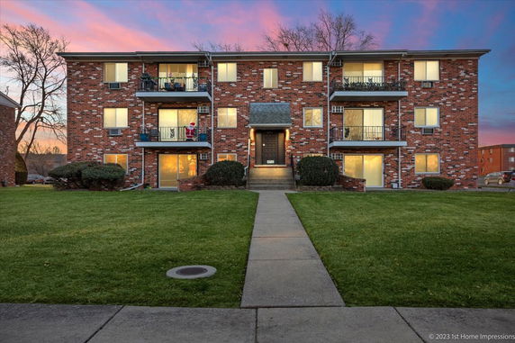 Front view of a three-story brick apartment building with balconies and a central entrance.