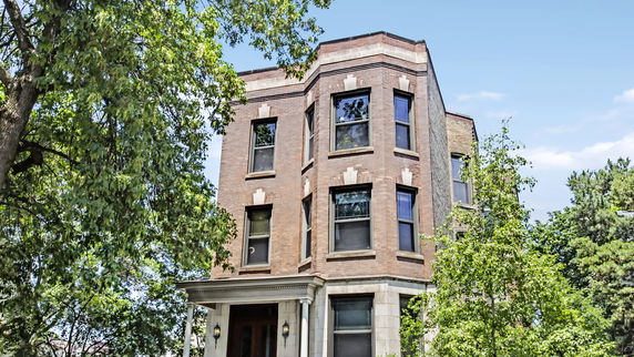 Front view of a multi-story brick house with large windows.