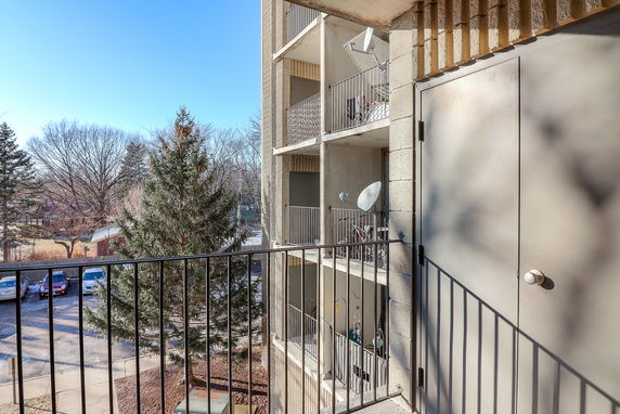 Balconies of an apartment building with a view of surrounding trees and parked cars.