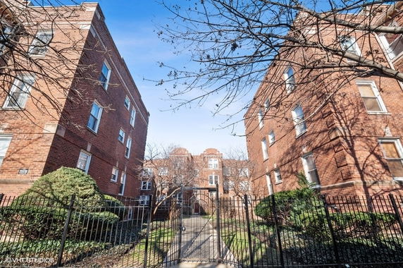 Front view of a multi-story brick apartment building with a gated entrance.