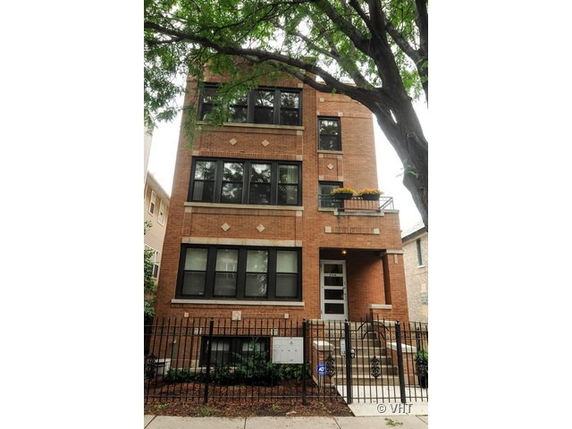 Front view of a three-story brick apartment building with multiple windows and a small entry porch.