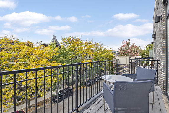 Balcony view overlooking a street with trees and buildings.
