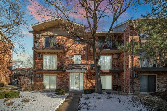 Front view of a three-story brick apartment building with balconies.