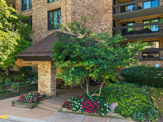 Front view of a brick building entrance with a pitched roof surrounded by greenery.