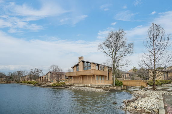 Front view of a house with wooden balcony overlooking a water body.