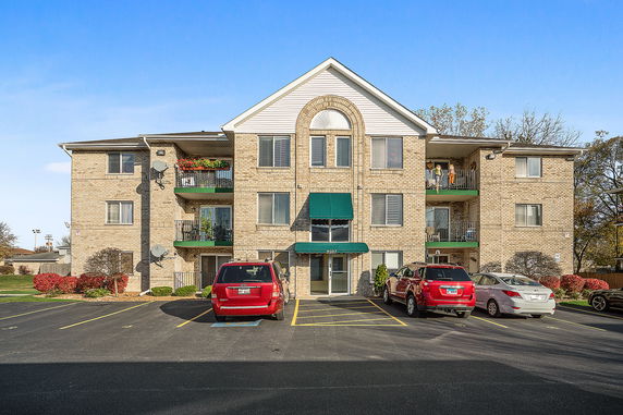 Front view of a three-story residential apartment building with multiple balconies and a parking area.